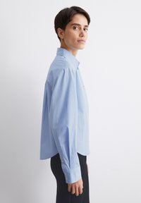 Lys blå skjorte med knaplukning, afslappet pasform, lange ærmer og manchet detaljer. Fremstillet af glat stof med et klassisk kravedesign.