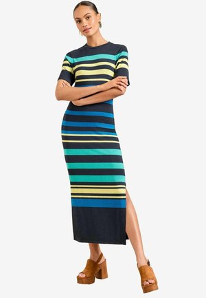 Tumed rõngaste mustriga maksime Kleid sinises, millel on horisontaalsed triibud rohelises, sinises ja kollases, külgmine lõhik ja lühikesed varrukad. Pruunid platvormkingad.