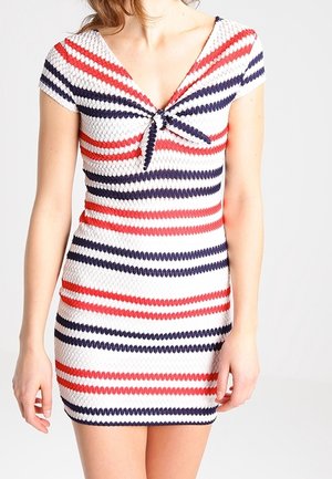 Femme portant une robe courte en maille texturée avec des rayures horizontales en zigzag rouge, blanc et marine et un petit nœud à l'avant au niveau de l'encolure.