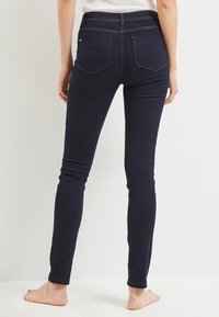 Jeans skinny blu scuro con vita alta, dotati di tasche posteriori e una consistenza in denim liscia e elastica. Nessun hardware o decorazione visibile.