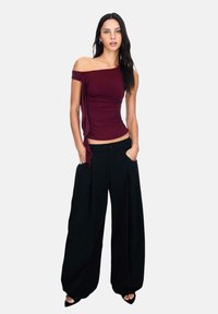 Bordo off-shoulder majica s nabranim detaljima sa strane, uparen s labavim crnim širokim hlačama. Glatka tkanina, opušteni kroj, minimalni akcenti.
