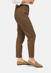 Brown tailored trousers with an elastic waistband and side pockets, featuring a slim fit and smooth texture. Paired with beige slip-on shoes.