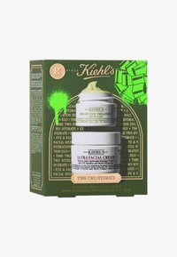 Il packaging di Kiehl's presenta uno sfondo verde con accenti dorati, che mette in mostra due barattoli di prodotto: una crema viso Ultra Facial bianca e un trattamento occhi cremoso verde.