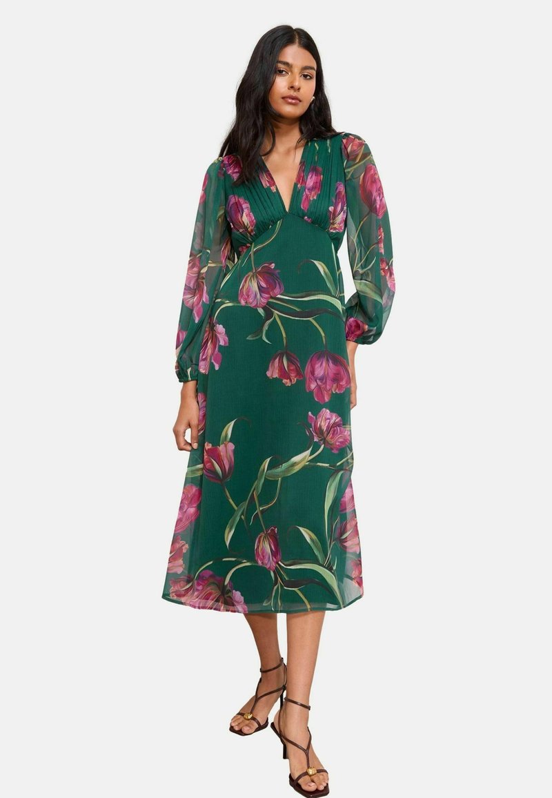 Pitkä vihreä mekko, jossa on syvä cpainsaluettelo, kukkakuvio pinkki- ja keltasisin, läpinäkyvät hihat ja midi-pituus.