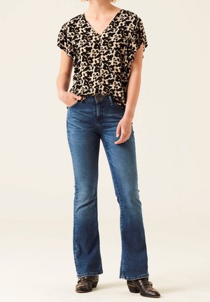 Black and beige short-sleeve top with a leopard print, paired with blue flared jeans. The outfit features a V-neckline and a relaxed fit.