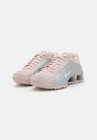 Zapatillas Nike en rosa y gris con un diseño elegante, detalles de malla y suelas de goma con un distintivo amortiguador en espiral en el talón.