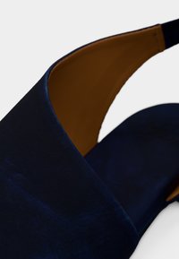 Κοντινό πλάνο μπλε ναυτικού σουέντ παπουτσιού slingback με ταμπά δερμάτινη εσωτερική επένδυση σε λευκό φόντο.