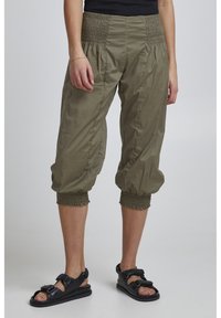 Pantaloni cropped verde oliva con vita arricciata, polsini elasticizzati e una texture leggera, abbinati a sandali neri con cinturini.