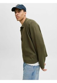 Polo-shirt à manches longues de couleur vert olive en tissu texturé, avec col et détails de boutons. Porté avec un jean bleu clair.