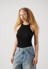 Melna ribota halter top ar pieguļošu dizainu, apvienota ar gaiši ziliem augsto jostasvietu džinsiem. Uzsvars uz kontūrām un tekstūrām.