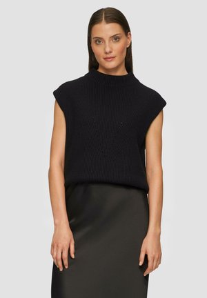 Pull noir en tricot avec un col montant et des manches courtes, présentant un motif en V texturé et un ourlet côtelé, associé à une jupe noire.