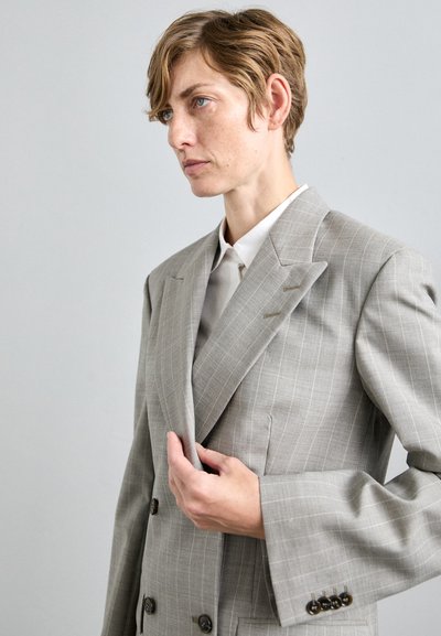 Gray double-breasted suit jacket with a pinstripe pattern, structured shoulders, and horn buttons. Accompanied by a collared shirt underneath.