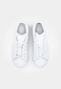 Pár bílých tenisek Adidas Stan Smith s tkaničkami, pohled zeshora na bílém pozadí.