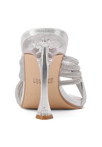 Sandalo alto con tacco in argento, con tacco trasparente, cinturini decorati e una finitura liscia e lucida. La suola è colorata in beige con un marchio inciso.