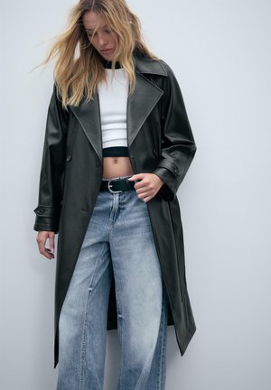 Manteau trench en simili cuir noir avec de larges revers, design à double boutonnage et manches longues, associé à un jean à jambes larges délavé et à un crop top.