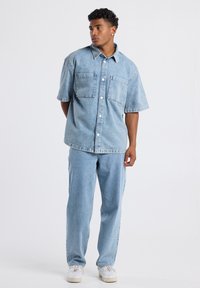 Vaaleansininen farkkupaita lyhyillä hihoilla, jossa on kaksi rintataskua, yhdistettyinä suoriin vaaleansinisiin farkkuihin. Pehmeä, tekstuuri pinnalla.