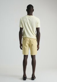 Camiseta amarilla clara y pantalones cortos amarillos claros, ambos de algodón. La camiseta tiene mangas cortas; los pantalones cortos cuentan con bolsillos traseros y un dobladillo limpio.