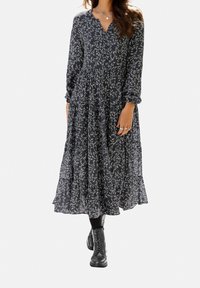 Svart blommig midiklänning med långa ärmar och V-ringning. Har en rynkad midja, en flödande kjol och vita blommönster överallt.