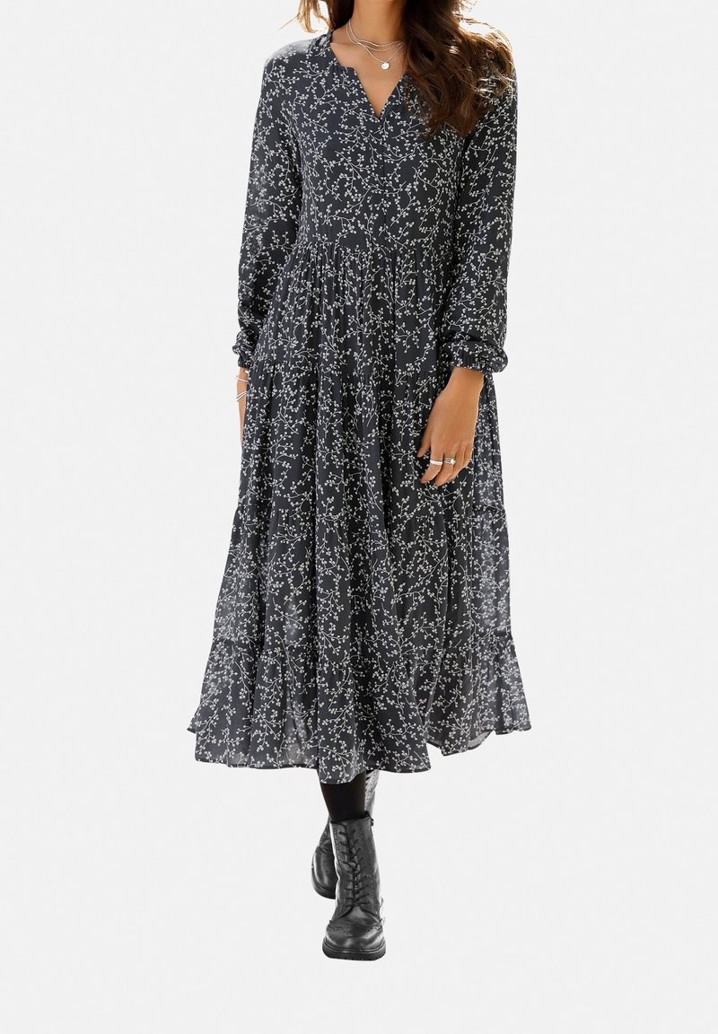 Svart blommig midiklänning med långa ärmar och V-ringning. Har en rynkad midja, en flödande kjol och vita blommönster överallt.