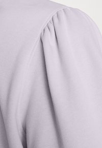 Světlý levandulový pulovr s měkkou, strukturovanou tkaninou. Má nabráné švy na ramenou pro zvýraznění detailů. Hladký povrch, neformální design.