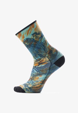 Calcetín con un patrón abstracto colorido en azul, naranja y negro, con punta y talón negros, exhibido en un maniquí de pie elevado.