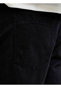 Nahaufnahme einer schwarzen Gesäßtasche an Jeansstoff, getragen mit einem weißen Hemd.