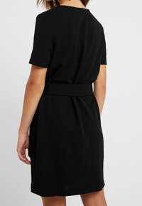 Czarna sukienka z krótkim rękawem, wykonana z miękkiego materiału, z paskiem w talii i prostym, czystym wzornictwem z minimalną ilością przeszyć.
