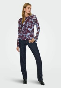 Langærmet top med en maroon bund og lyseblå blomster mønstre, parret med mørk denim jeans og sorte spidse ankelstøvler.
