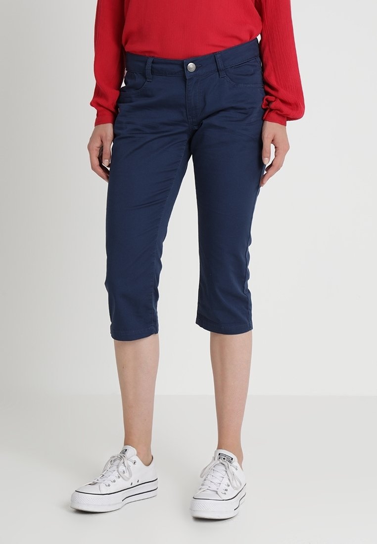 Pantalons cropped bleu marine en tissu doux, dotés d'un design à cinq poches, de passants de ceinture et d'une fermeture à bouton argenté. Portés avec des baskets blanches.