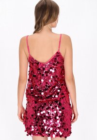 Rózsaszín flitteres ruha, mély hátkivágással, vállpántokkal, testhez simuló sziluettel és fényvisszaverő flitterekkel borított anyaggal.