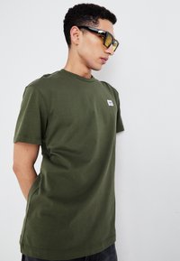 Olivengroene katoenen t-shirt met een ronde hals en korte mouwen. Voorzien van een klein merkembleem op de linkerborst en een ontspannen pasvorm.