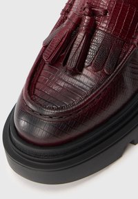 Bordeauxkleurige leren schoen met een gestructureerd krokodillenleren patroon, met een ronde neus en een zwarte rubberen zool. Accent met kwastjes.