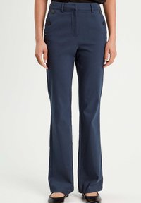 Navyblaue, maßgeschneiderte Hose mit hohem Bund, ausgestellten Beinen und dekorativen schwarzen Knöpfen an den Seiten Taschen. Glatte Textur.