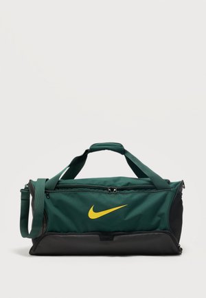Sac polochon vert foncé et noir avec un swoosh Nike jaune, poignées supérieures, bandoulière ajustable et compartiments zippés sur un fond clair.