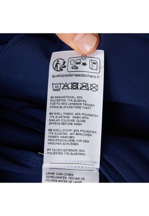 Mørkeblå stofmærke med vaskeanvisninger og materialedetaljer. Tekst på flere sprog: 83% polyester, 17% elastan.