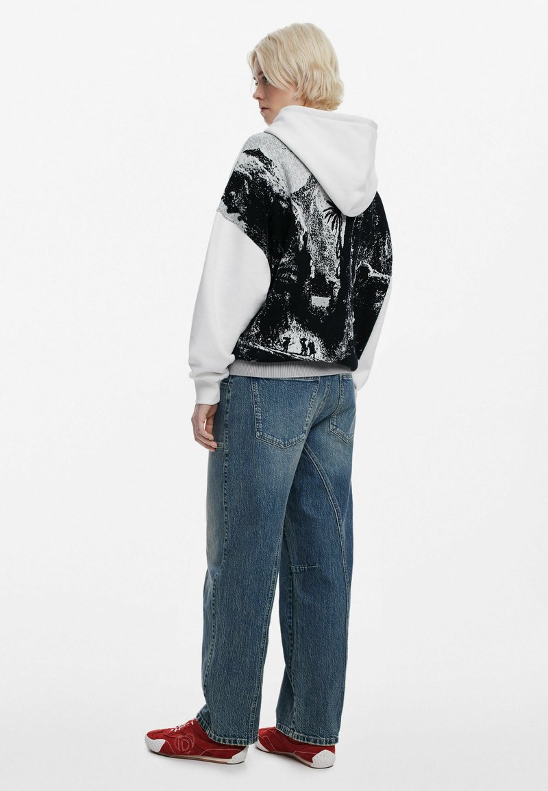 Sort og hvid trykt hoodie med en frontlomme og snoretræk i hætten, båret med løstsiddende blå denimjeans og røde sneakers.