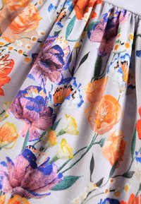 Jupe florale présentant un motif varié de fleurs orange, violettes et bleues sur un fond gris clair ; tissu doux avec une texture plissée.