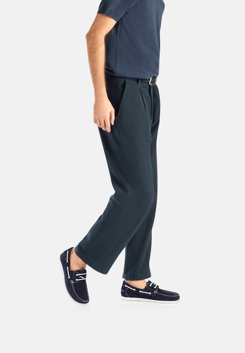 Navy-Blaues Kurzarmhemd, dunkelgrüne gefaltete Hose und dunkelblaue Bootsschuhe mit weißen Nähten und Schnürsenkeln, von der Seite gezeigt.