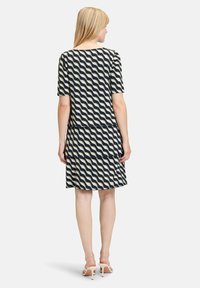 Sukienka z krótkim rękawem w kolorze granatowym z falistym wzorem w kremowym odcieniu. Fason dopasowany w talii, zwiewny dół, wykonana z miękkiego, elastycznego materiału. Długość do połowy uda.