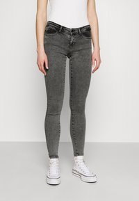 Jeans negros ajustados con un acabado desgastado, cinco bolsillos y presillas para cinturón, combinados con zapatillas blancas de caña alta.