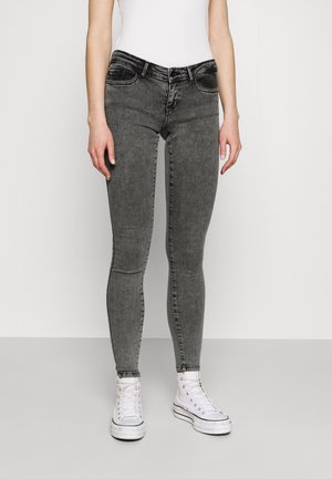 Jeans negros ajustados con un acabado desgastado, cinco bolsillos y presillas para cinturón, combinados con zapatillas blancas de caña alta.