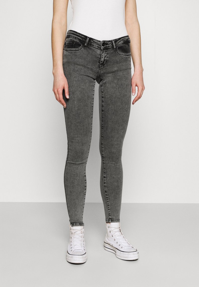 Jeans negros ajustados con un acabado desgastado, cinco bolsillos y presillas para cinturón, combinados con zapatillas blancas de caña alta.