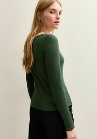 Groene geribbelde long sleeve top met een aansluitend ontwerp en ronde halslijn, gedragen met donkere jeans, die de gestructureerde stof en gestroomlijnde silhouet toont.