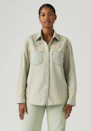 Jasnozielona koszula dżinsowa z zapięciem na guziki, dwoma kieszeniami na piersiach i wzorem na szczycie w stylu western. Miękka, lekko wyblakła faktura.