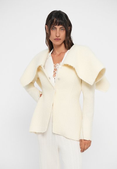 Blazer branco texturizado com um colarinho oversized, apresentando um fecho frontal por botão, mangas longas e uma silhueta estruturada.