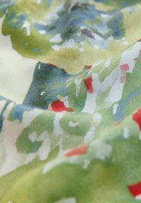 Ein Textilstoff mit einem lebhaften, abstrakten Muster in Grüntönen, Blau und Rot. Die Oberfläche wirkt glatt und hat eine weiche Textur.