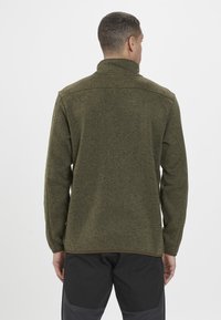 Olivgrön fleecejacka med hög krage, texturerad yta och avslappnad passform. Har en slät nederkant och långa ärmar.