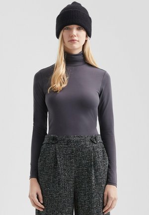 Langsleeve, strakke grijze top met een hoge kraag, gecombineerd met gestructureerde zwart-wit gemusterde broek en een zwarte gebreide beanie.