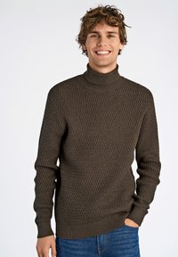 Brauner gestrickter Rollkragenpullover mit einem strukturierten Rautenmuster, gerippten Bündchen und Saum, kombiniert mit blauen Jeans. Lässiger, figurnaher Stil.