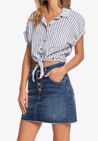 Chemise à boutons rayée, coupée, en blanc et gris. Jupe en denim bleu avec des boutons sur le devant et un ourlet effiloché. Comprend une poche sur le côté.